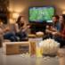 People gathering in a living room watching a sporting event and enjoying Snappy popcorn white Snap-Paks.