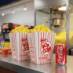 Classic red and white 130 oz popcorn tub at a theater concession stand with a can of Coke.